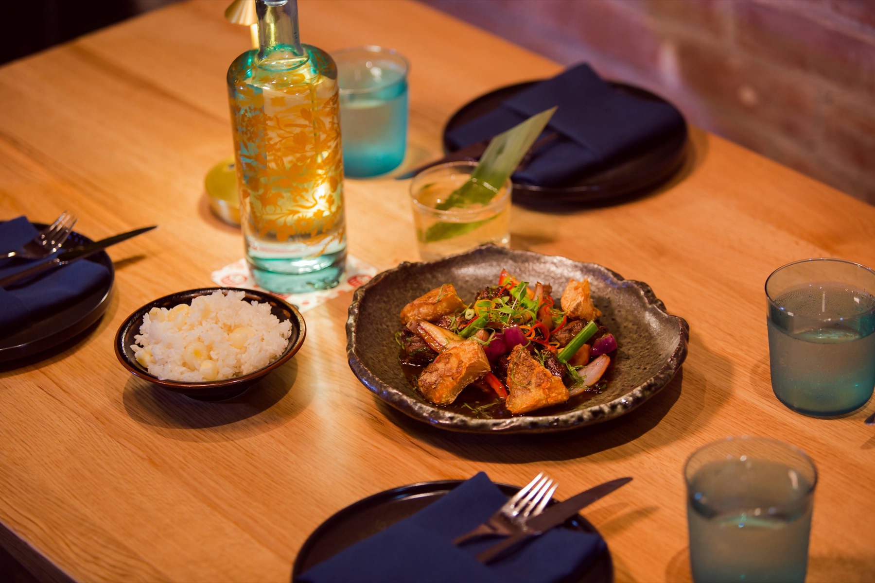 A Nikkei dinner set for guests, with rice, a shared plate and cocktails on a wooden table